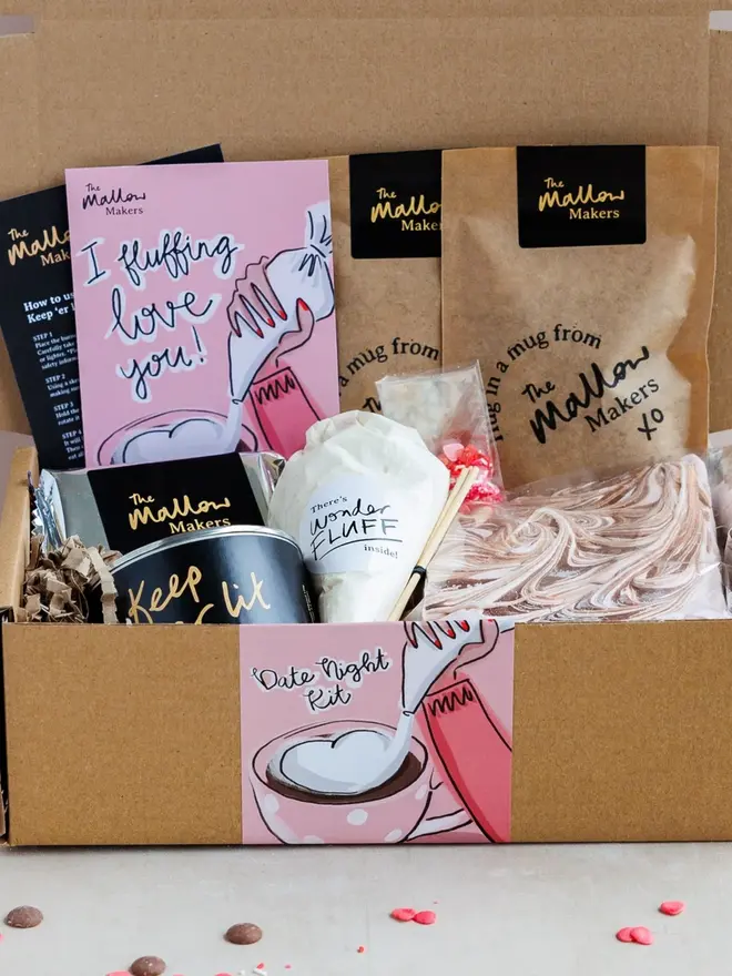 Date Night S'mores And Hot Chocolate Kit, the kit fully packed in to a box on a marble surface. It is surrounded by more small valentines sprinkles. 