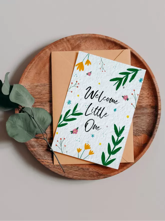 'Welcome Little One' New Baby Plantable Card with Floral Illustrations on a wooden tray next to eucalyptus