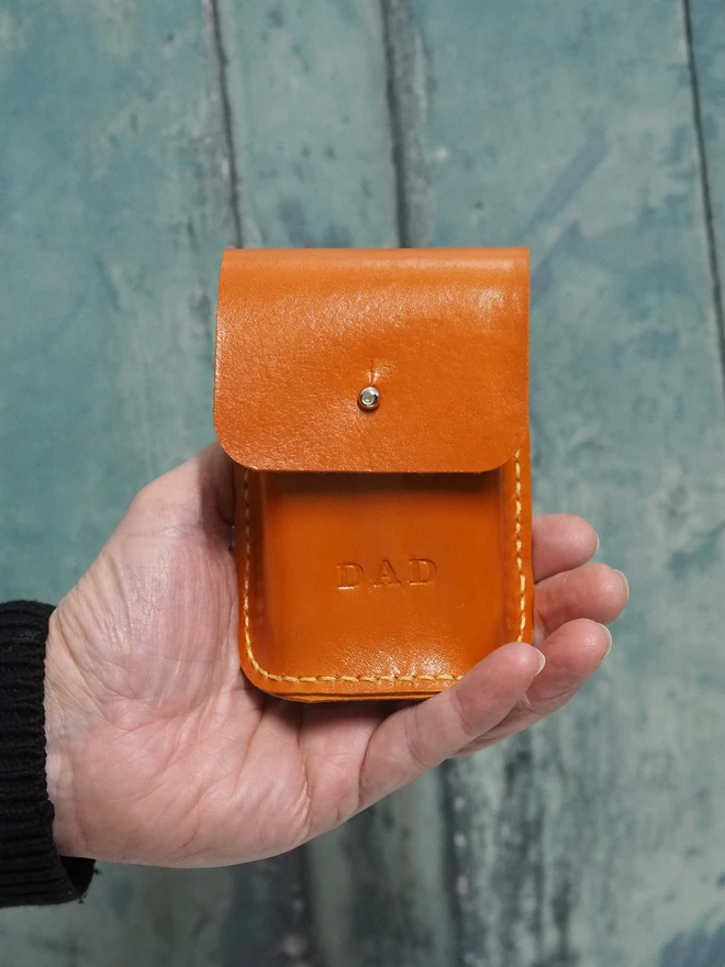 Personalised orange leather playing card holder. A leather case to hold a pack of cards sits in a hand. The case is personalised with the name DAD