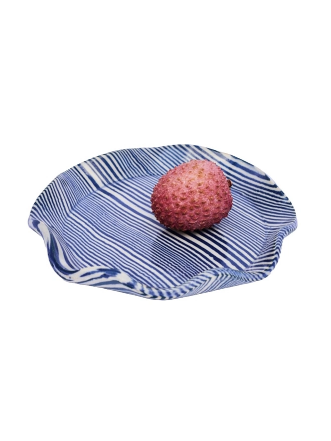 Striped Trinket Dish, a colourful trinket dish sitting on a white surface against a plain backdrop. It is accompanied by some lychees. 
