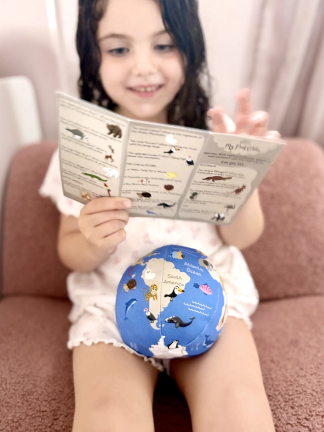 First globe soft toy on the legs of little girl. She is holding the paper guide that comes with it