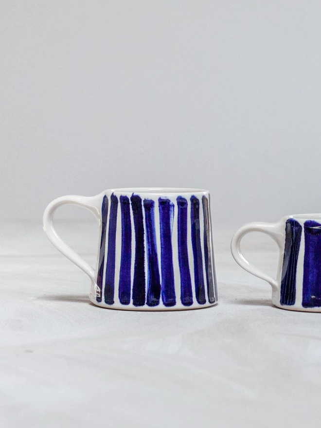 Gloss handmade mug with cobalt blue hand-painted stripes seen in two sizes.