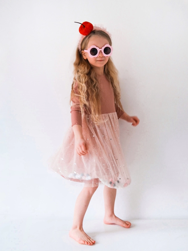 Young girl posing wearing sunglasses and a pom pom tutu dress