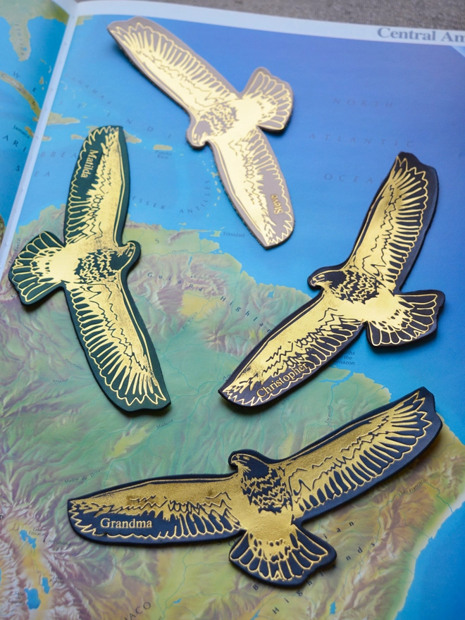 flying gold embossed foil eagle bird leather bookmarks on a large open atlas book depicting a map of Central America by natthakur