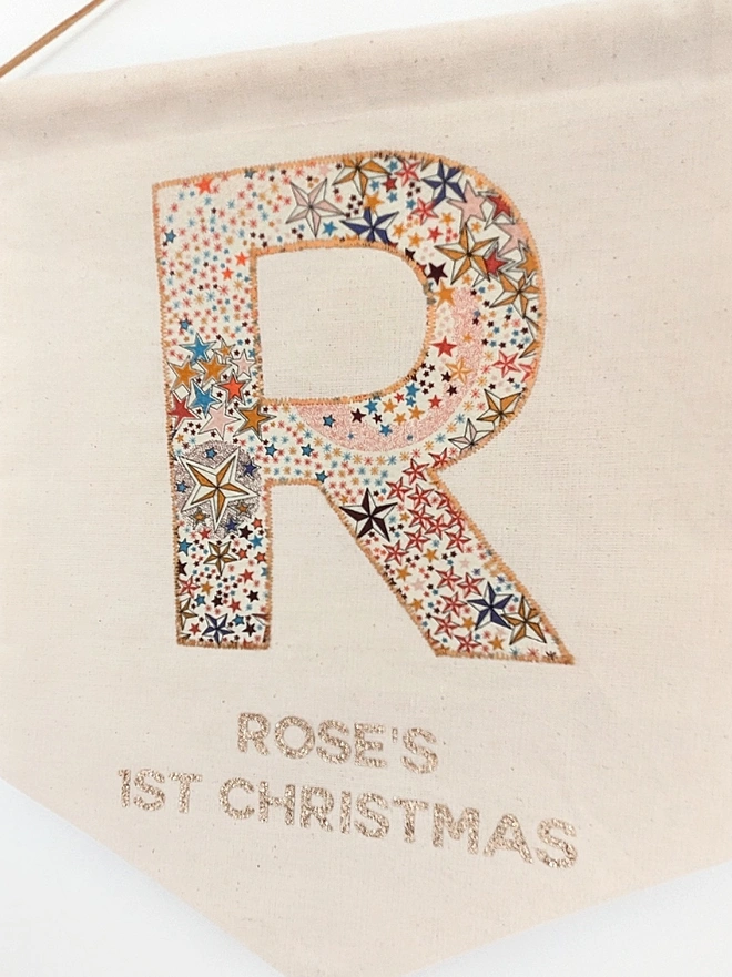 close up of fabric banner personalised with Liberty fabric initial and babies name followed by 1st Christmas underneath