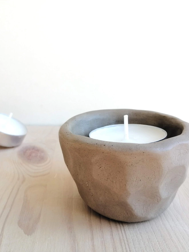 Handmade tealight holder containing tealight on a wooden surface. Tealight in the background