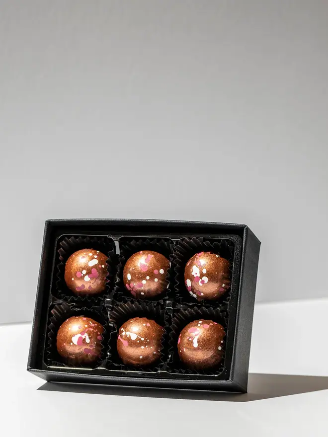 Raspberry gin truffles in a black box on a white table, pack of 6. 