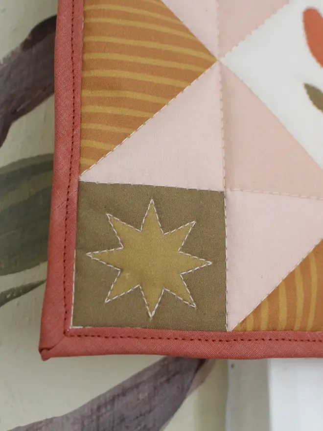 tulip quilt wall hanging. a close-up corner of a patchwork quilt with a pink star pattern in the centre.