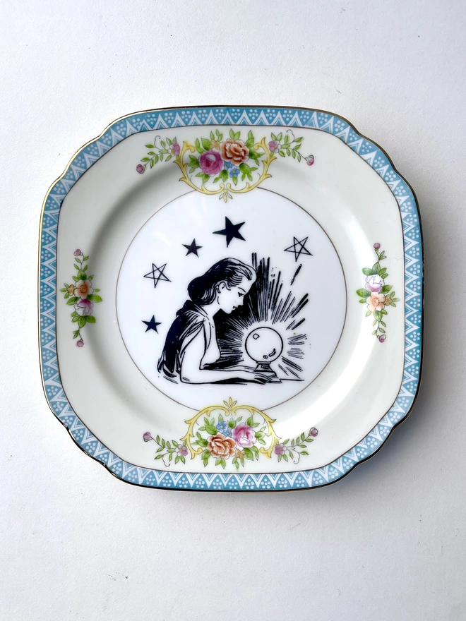 a vintage ornate plate with a pink floral border detail, in the centre i have printed a vintage black and white illustration of a pretty fortune teller reading a crystal ball