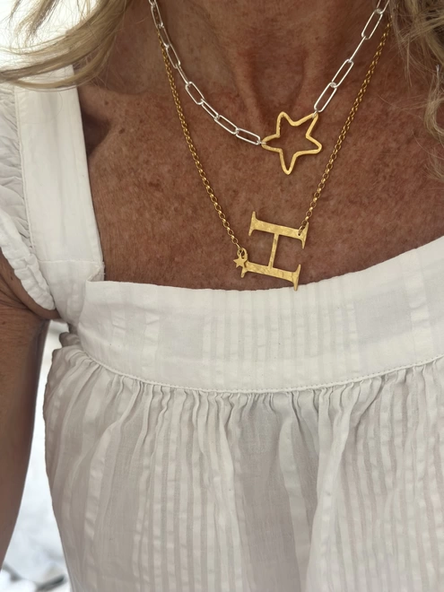 model wears rough hewn open star charm in gold on a sterling silver paperclip chain and large gold H letter charm on gold chain with gold mini star