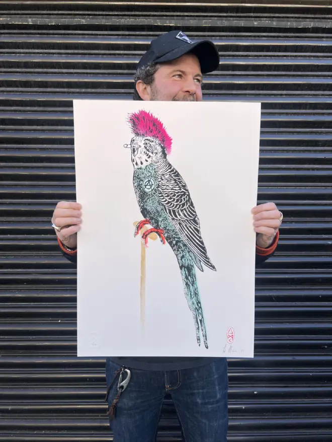 Punk budgie lino print, with symbols, coloured with blue and pink paint with on a white background. 