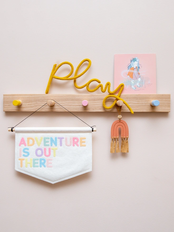 White felt banner with the words "Adventure is out there" written on it in a mix a soft pastel colours