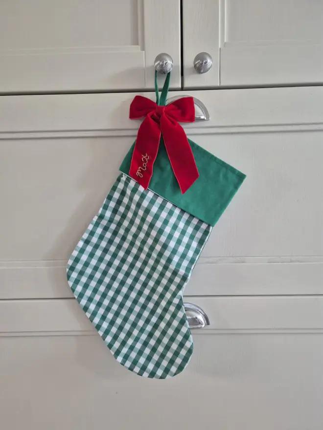 green gingham stocking with red velvet bow, embroidered with a name