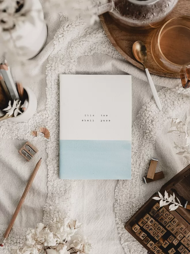 soft blue and white wellness journal with 'this too shall pass' typed on the cover