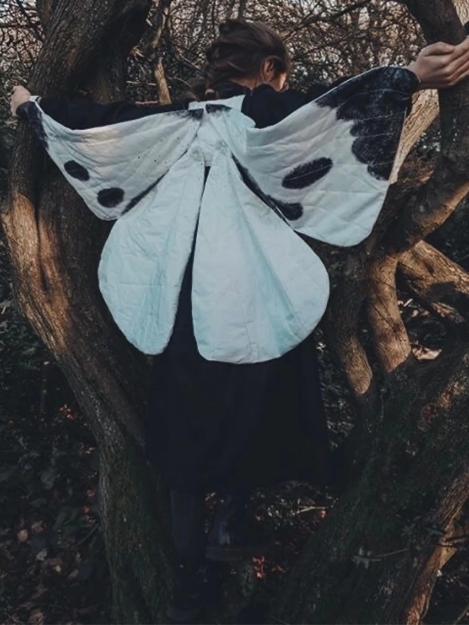 A child climbing a tree wearing black and white butterfly wings