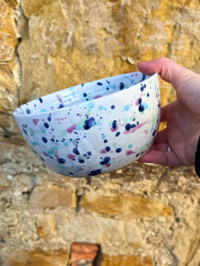Sweetpea Ramen Bowl, a colourful ramen bowl held by a person in front of a brick backdrop. 