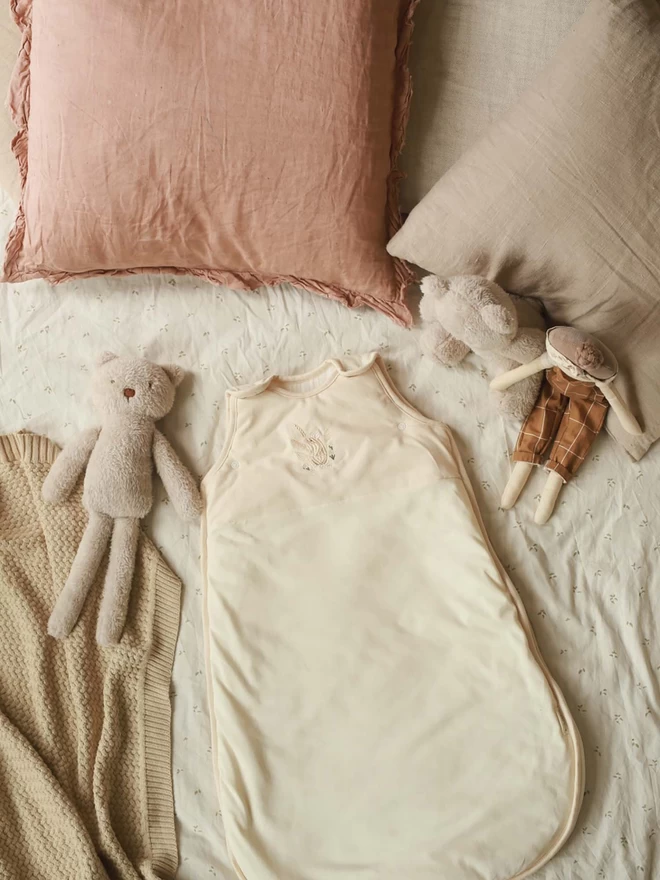 Baby sleeping bag with mouse embroidery placed on a bed with stuffed toys