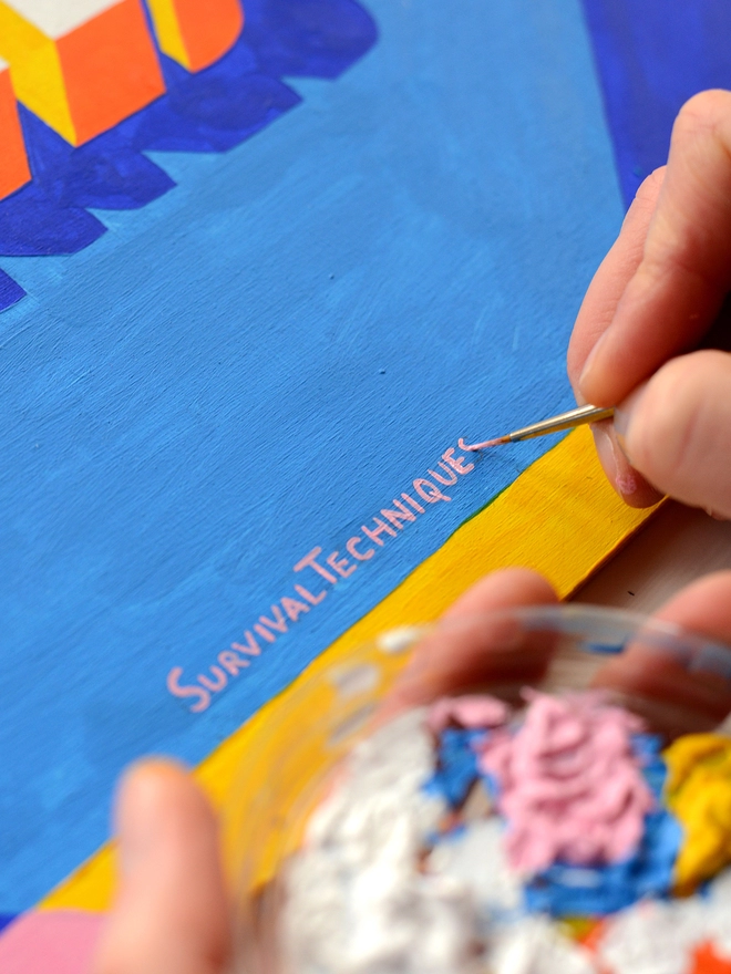 Close up of artist's hand painting the signature on a canvas of the words Survival Techniques