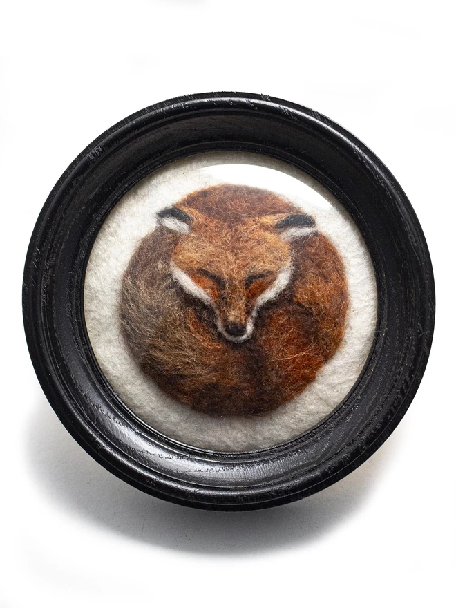 A needle-felted fox portrait in a round black frame