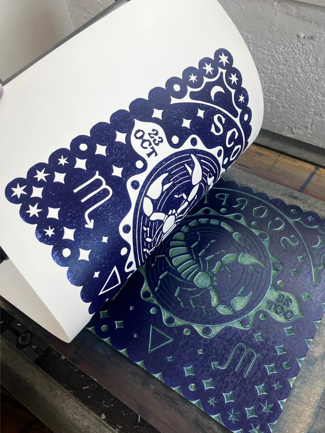 scorpio zodiac linocut. a linocut scorpion and zodiac symbols printed on a blue background.