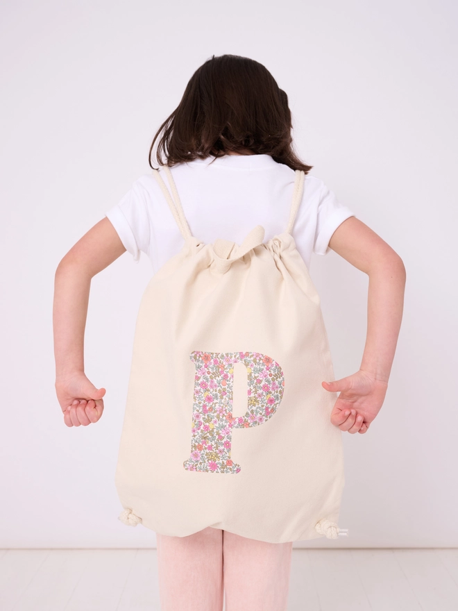 a 5 year old girl wearing a Magnificent Stanley Personalised Liberty Print Drawstring Backpack with her initial on in floral print