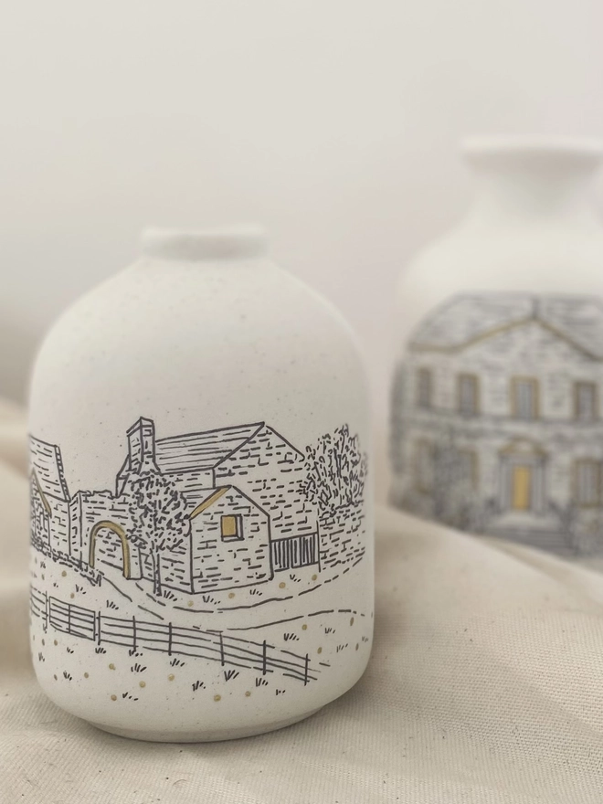 Two ceramic vases with a black line drawing of a wedding venue with metallic gold painted highlights