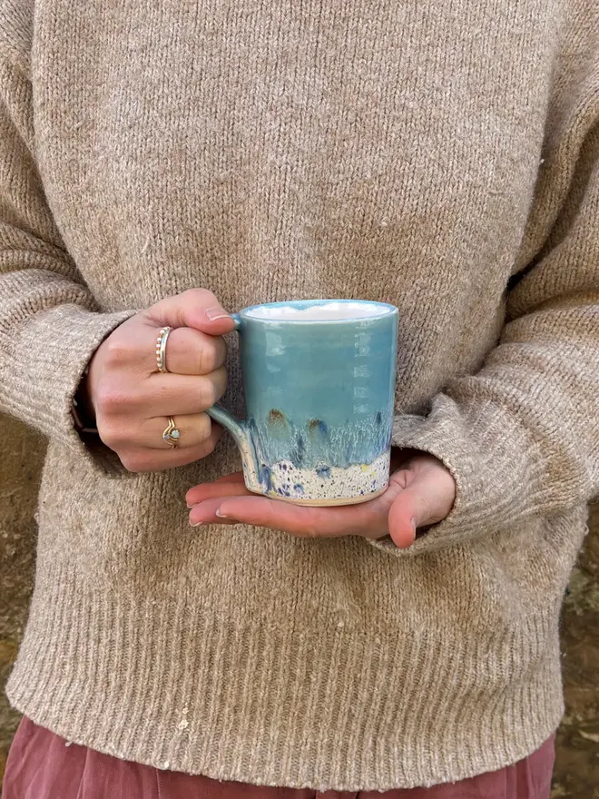 Shoreline Standard Mug, a colourful mug held in front of a person in a jumper. 