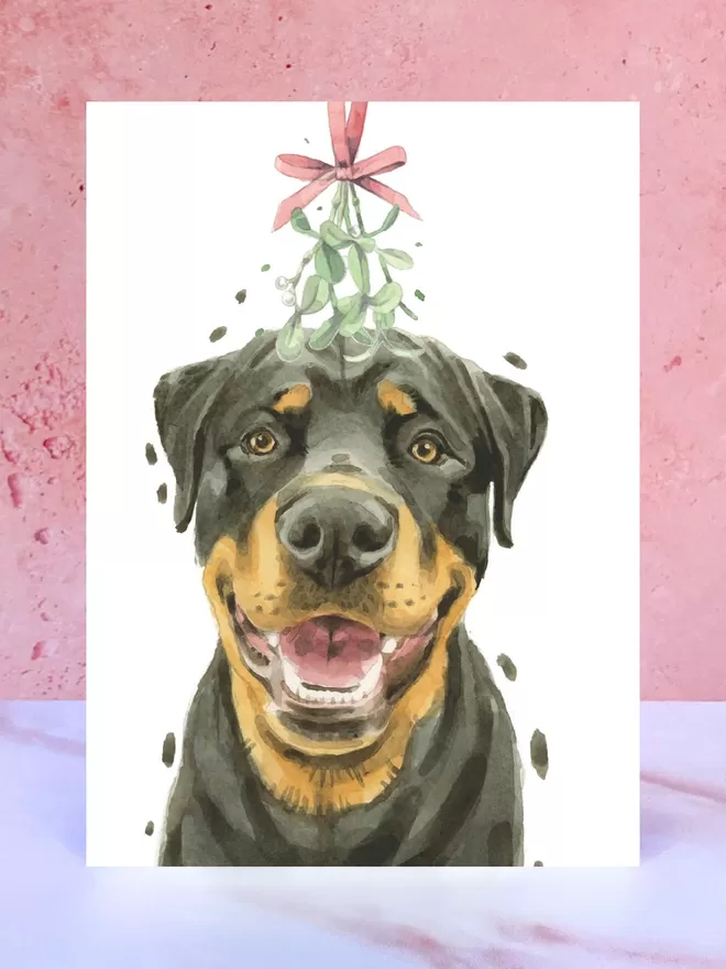 A Christmas card featuring a hand painted design of a Rottweiler, stood upright on a marble surface.