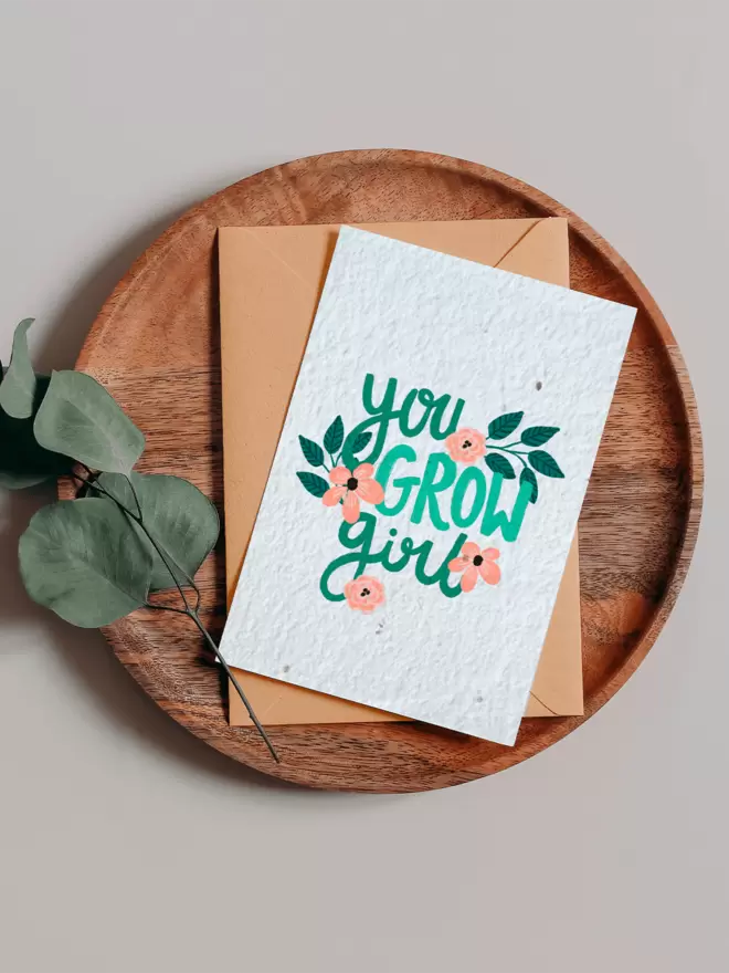 Seeded Paper Greeting Card featuring floral illustrations and ‘You Grow Girl’ in the centre on a wooden tray next to a Eucalyptus branch