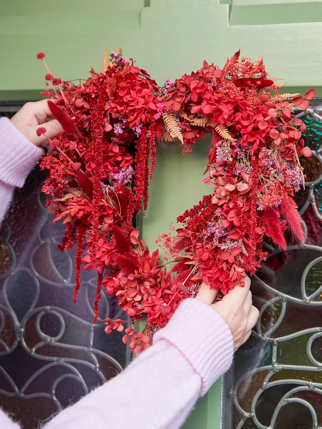 Red floral heart wreath being hung on a green door with stain glass windows