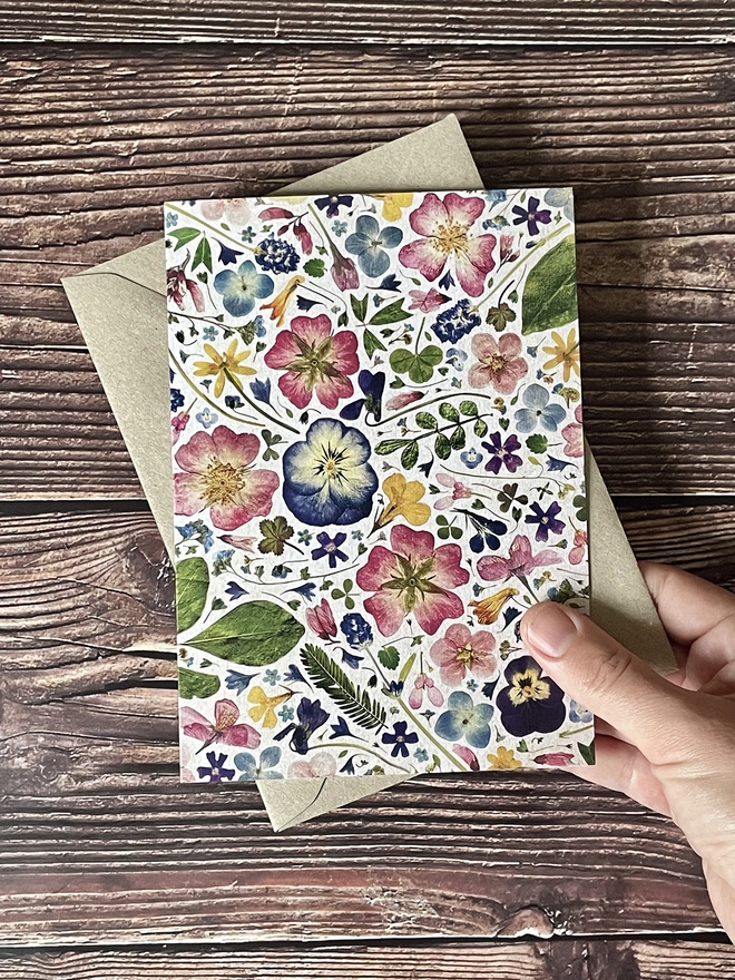 Hand Holding Greetings Card with Digitally Printed Pressed Flower Design - Brown Kraft Envelope - Brown Wooden Background