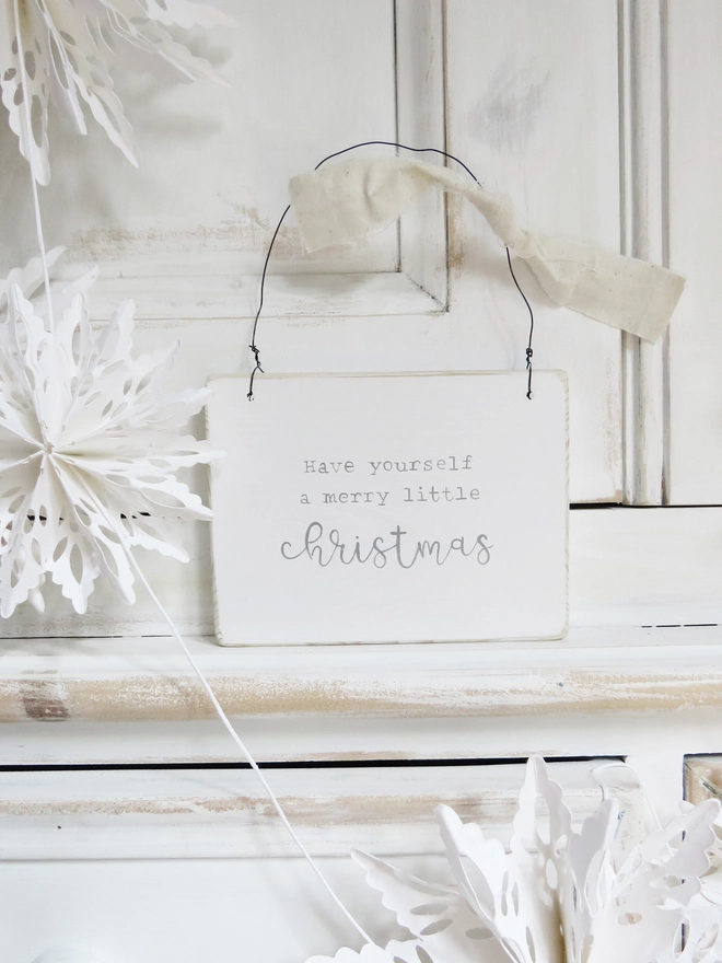 white wooden sign painted with a merry little Christmas message hung on wire and decorated with ribbon