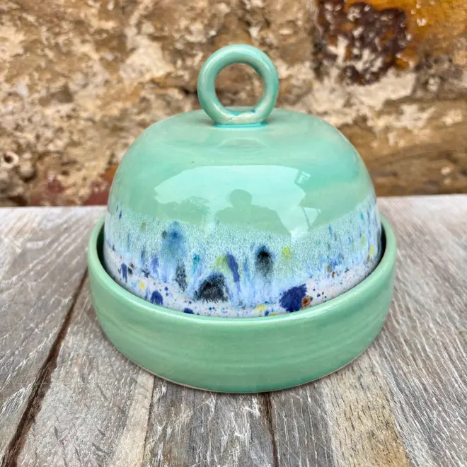 Shoreline Butter Dish, a colourful butter dish placed on a wooden surface against a brick wall. 