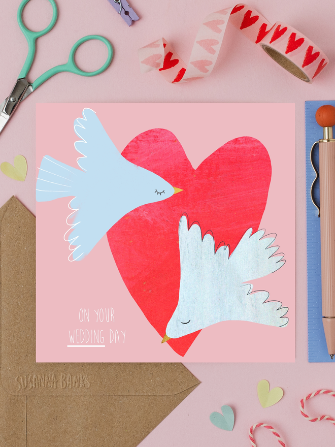 illustrated doves wedding card. card photographed on table with assorted crafting items.