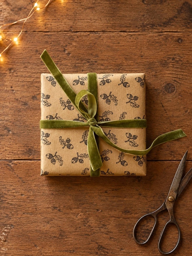 a present wrapped in a hand stamped kraft paper tied with a pretty sage green velvet bow