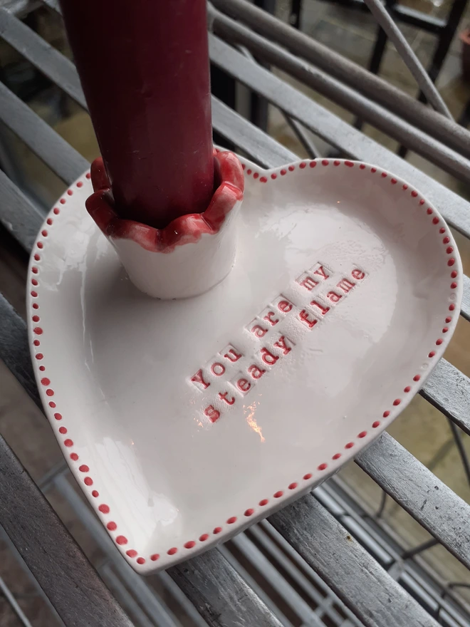 Valentine’s ceramic candle holder with a built-in taper candle cup, featuring red hand-painted details and the message ‘You are my steady flame’ in the centre of the heart dish.
