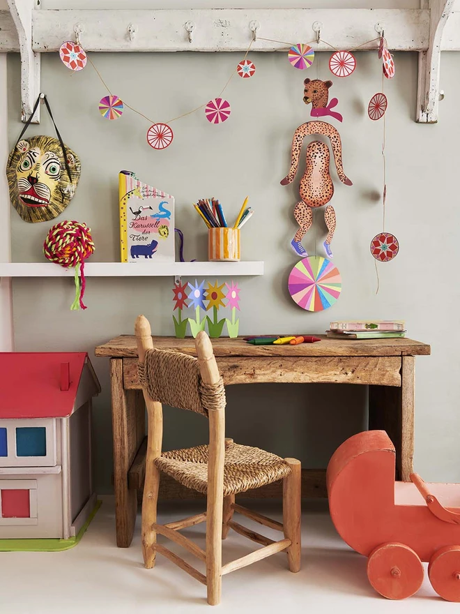 A hanging card mobile of a cheetah, haing over a cute kids desk and alongside vintage dolls house and wooden pram