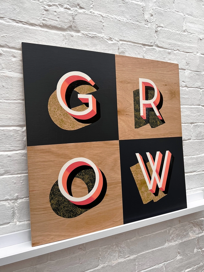 GROW hand painted sign in coral, dark grey and chartreuse, against a white brick wall, at an angle. 