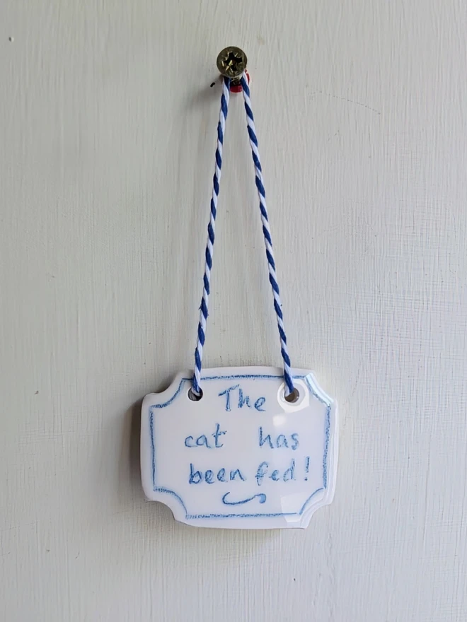 the cat has been fed sign in blue and white ceramic hanging decoration