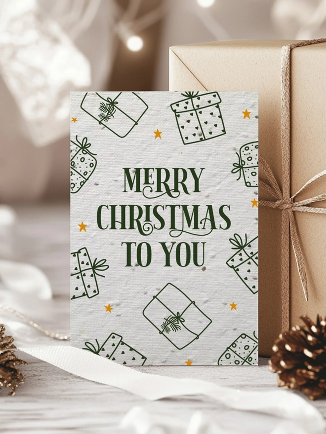 Christmas Card with 'Merry Christmas To You' with presents around the edge of the card. The card is surrounded by presents with gold ribbon