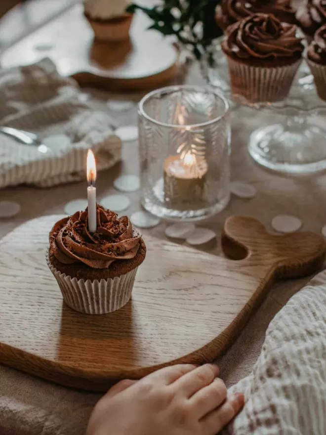 a chocolate cupcake with a lit candle resting on a whale wooden serving board