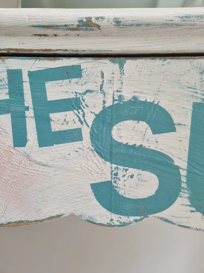 A painted dressing table in white and pale pink with large florals in blues and mauves and text in turquoise that reads 'turn your face to the sun'. The whole piece is distressed in the shabby chic style.