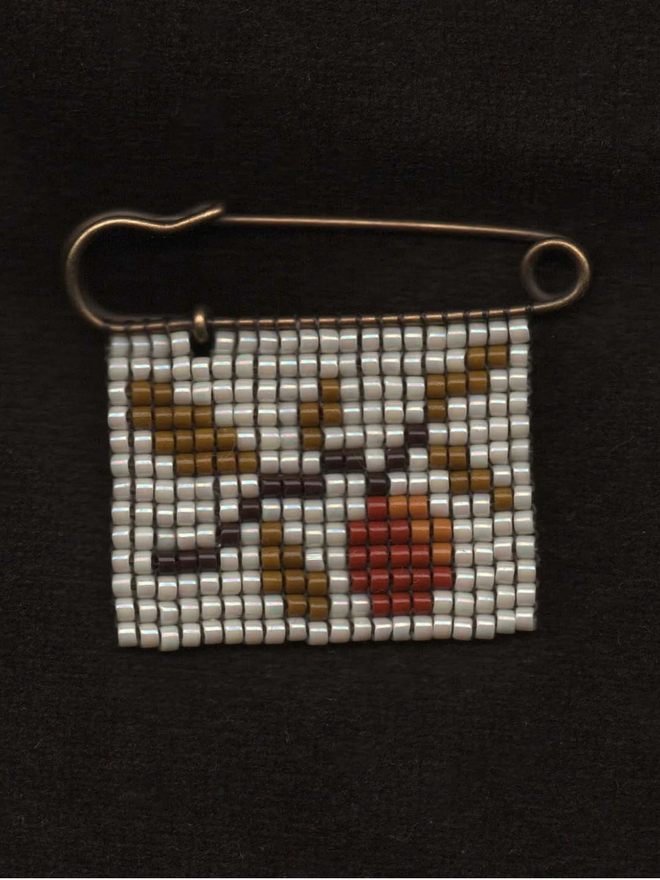 'Flora VI' Tiled Beaded Orange Pin. a beaded pin badge with an orange tree branch on a pearl background.