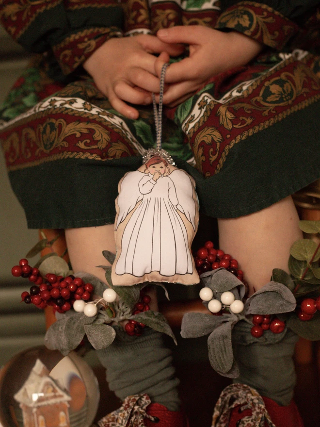 an angel decoration perfect for a Christmas tree made from printed fabric plush with a tinsel halo being held by a little girl with red hair