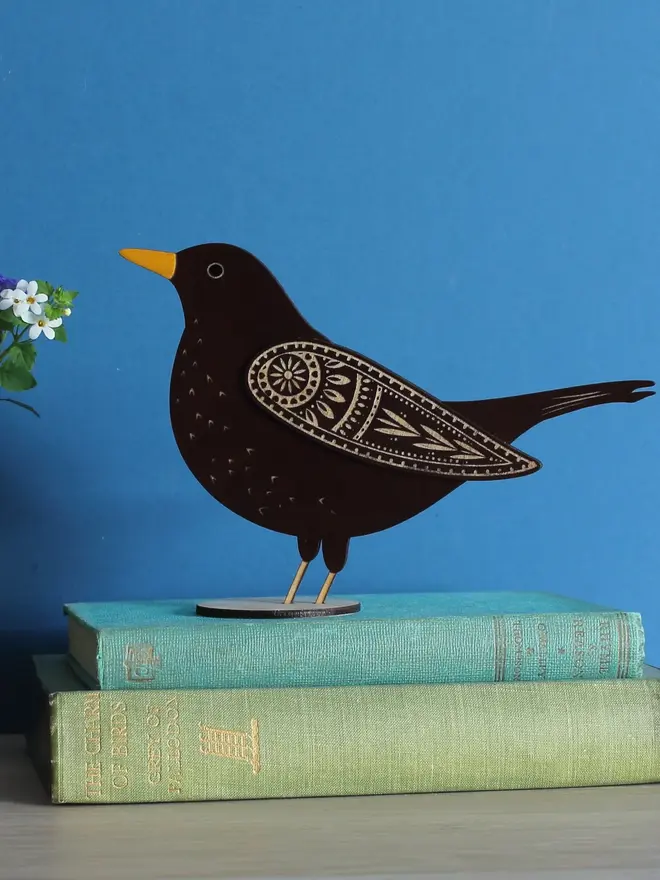 Standing Wooden Female Blackbird, black wooden bird standing on a book on a wooden platform. 