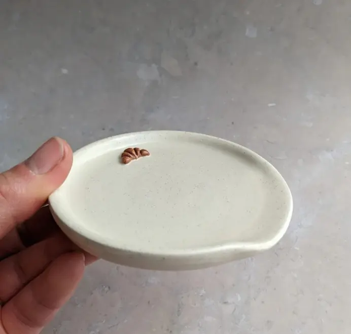 Croissant stoneware spoon rest in vanilla bean glaze against a grey marble background.