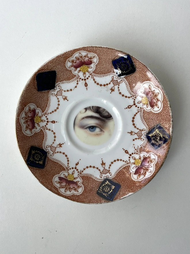 vintage plate with an ornate border, with a printed vintage illustration of an eye in the middle