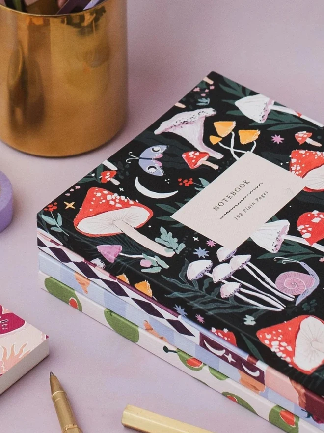 Mushrooms Notebook beside a gold pen pot
