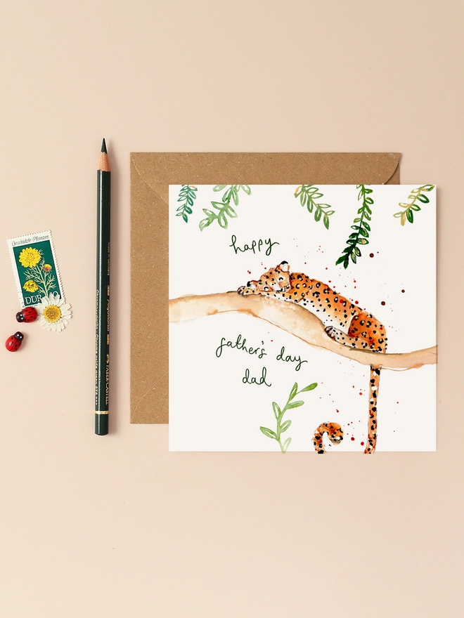 An illustration of a relaxed leopard lounging on a tree branch, exuding a laid-back vibe. The leopard's eyes are half-closed, and its body is stretched out comfortably. Above the scene, the handwritten message "Happy Father's Day Dad" adds a personal touch. The card's design combines playful animal imagery with a heartfelt sentiment, perfect for Father's Day.
