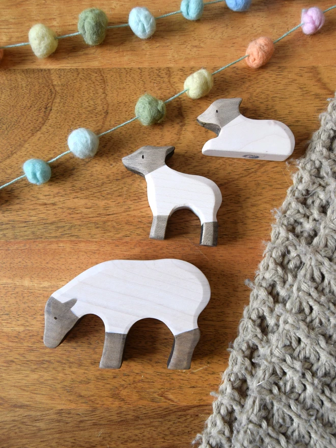 Wooden toy black and white sheeo and lambs laying on table with blanket and pom pom garland